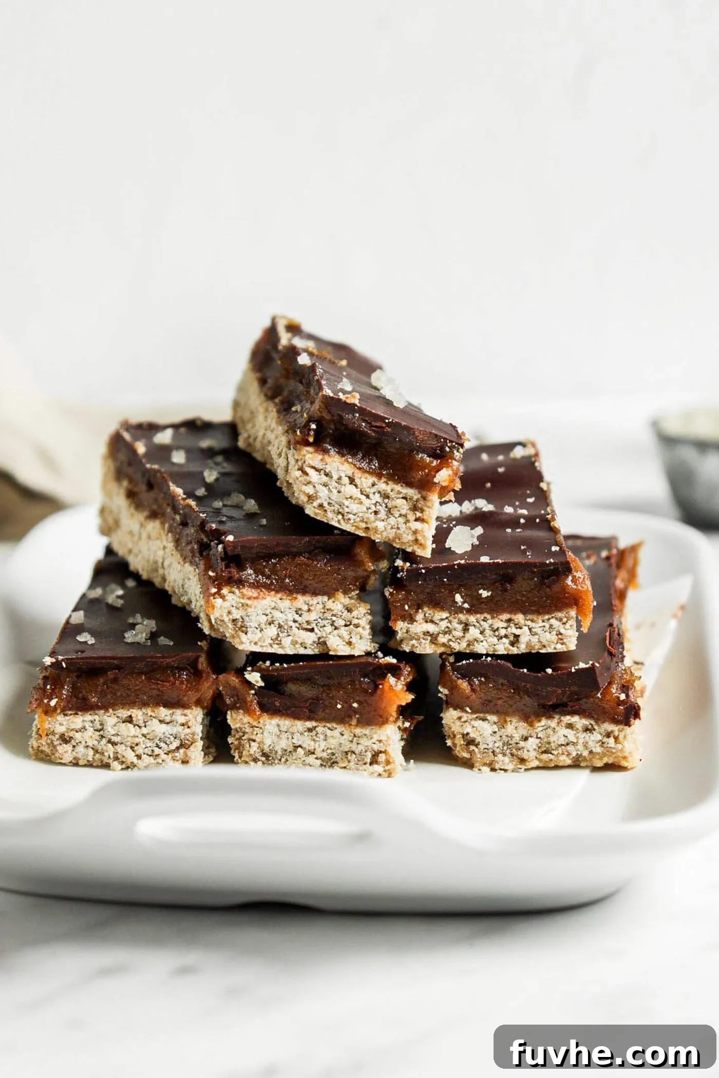 Stack of 6 homemade Twix-style bars with a shortbread, caramel and chocolate layer on a small dish.
