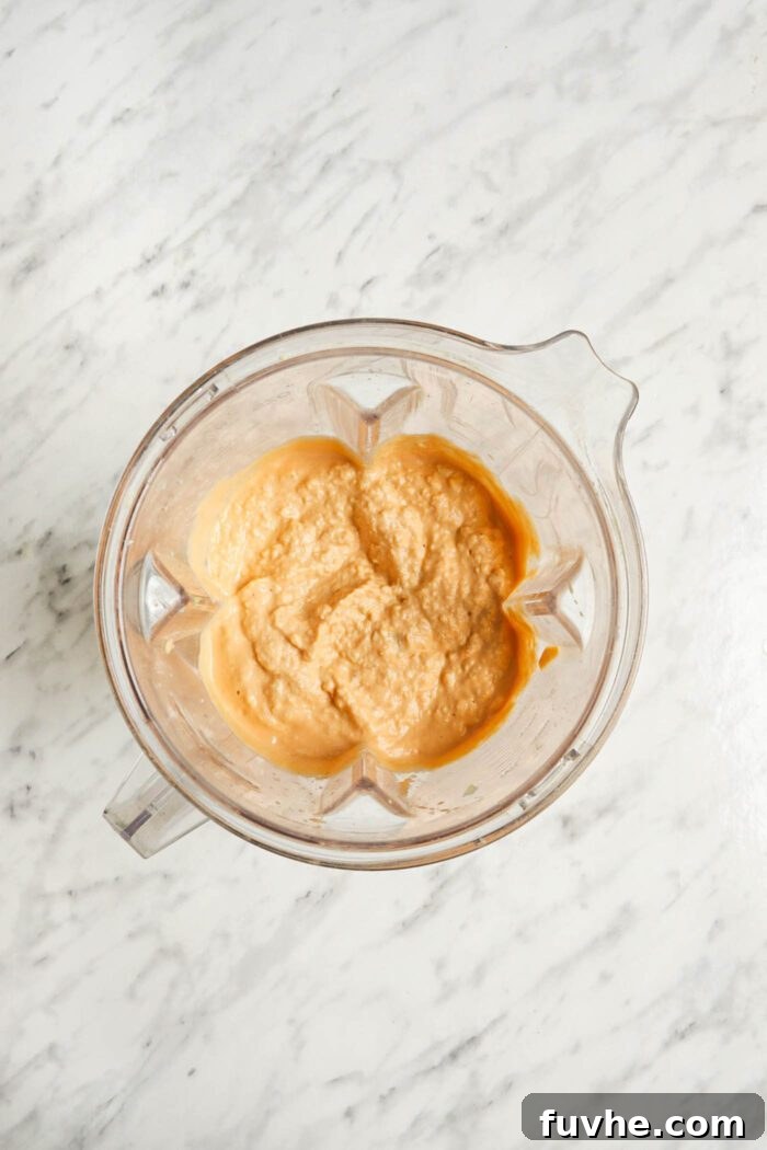 Chunky vegan buffalo dip, with visible artichoke pieces, in a large blender container after pulsing.