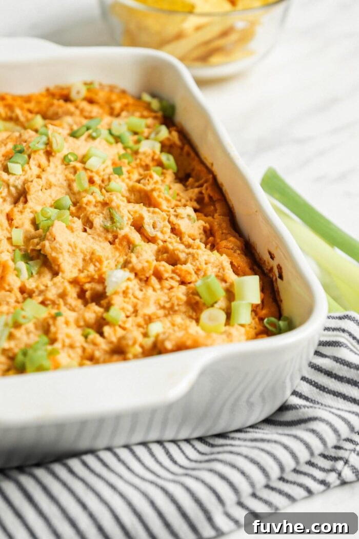 Close-up of creamy vegan buffalo dip in a white ceramic baking dish, garnished with fresh green scallions, ready to be served.