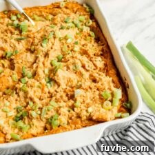 Close up of creamy vegan buffalo dip in a white ceramic baking dish, topped with fresh scallions.