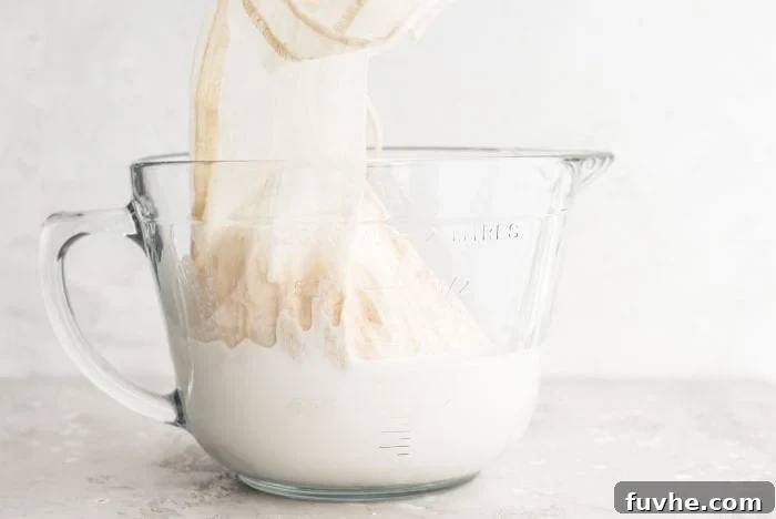Blended almond milk and a nut milk bag in a large glass measuring cup.