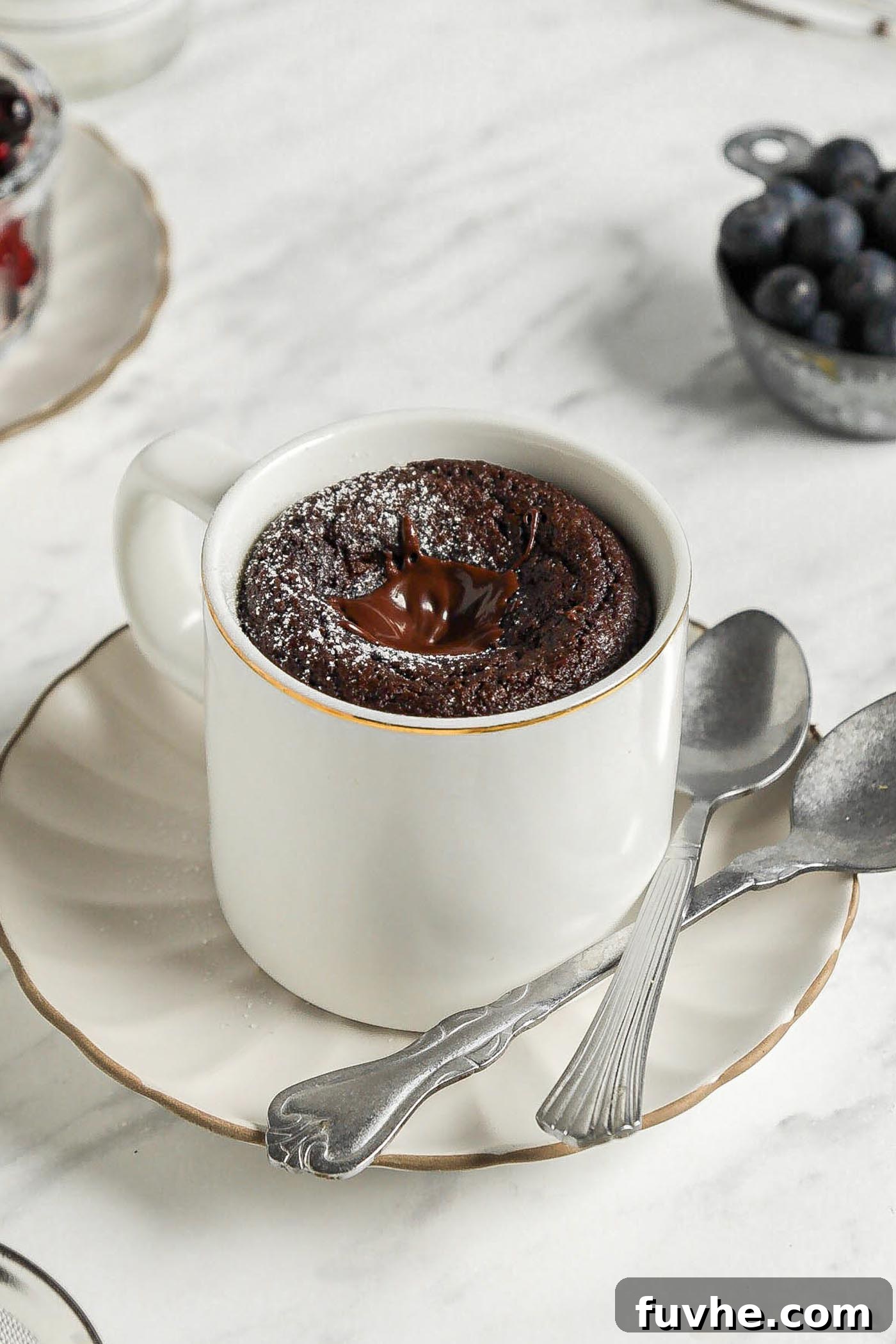 Mugful of Vegan Chocolate Bliss 2 A freshly made vegan chocolate mug cake presented on a small plate, with two spoons resting beside it, inviting indulgence.