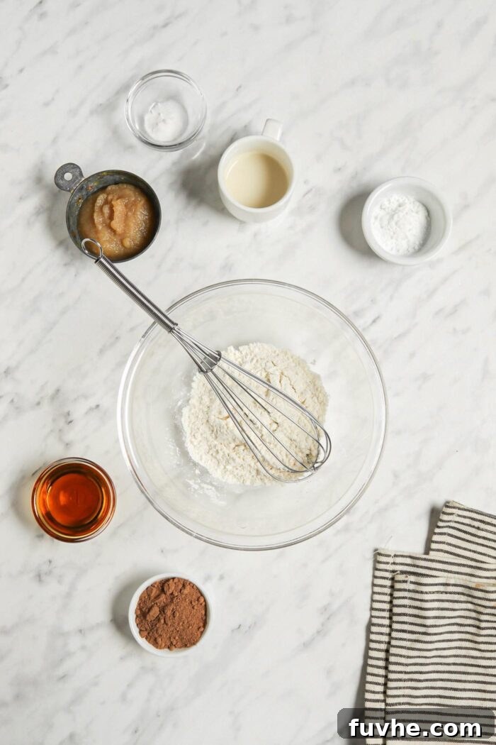 Mugful of Vegan Chocolate Bliss 4 Dry baking ingredients, including flour, cocoa powder, and baking powder, are shown expertly mixed together in a clear glass mixing bowl, ready for the next step.