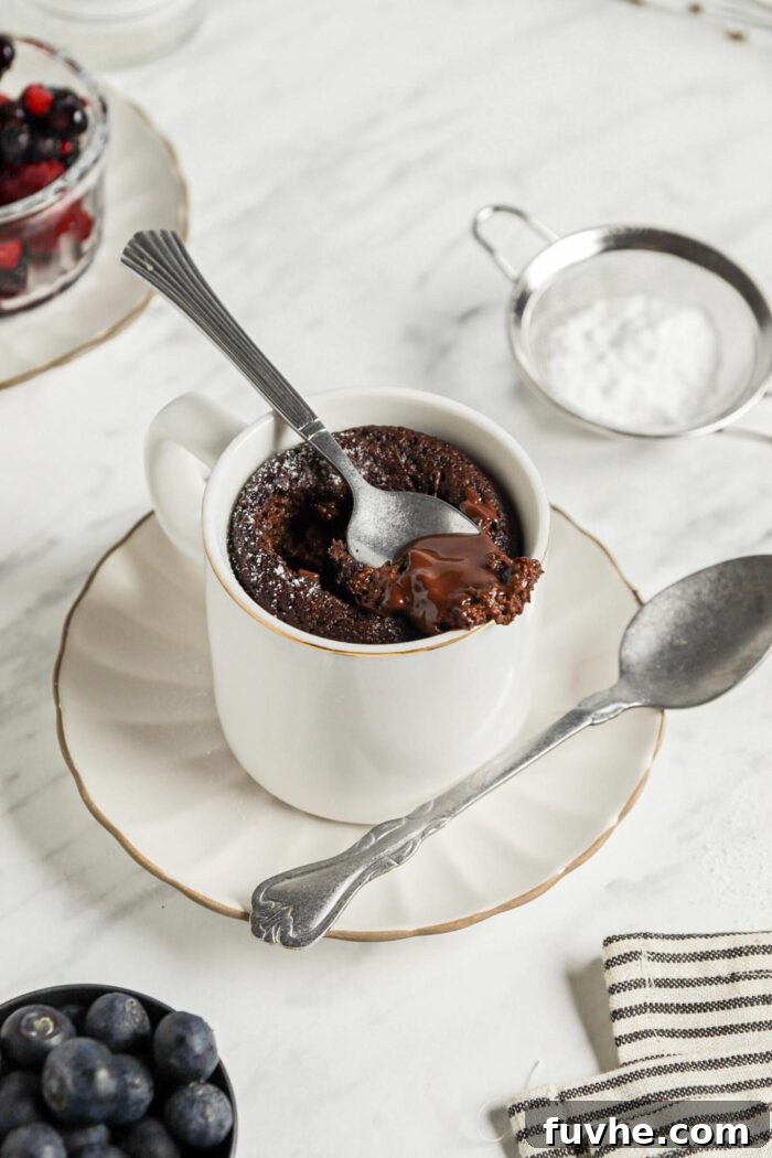 Mugful of Vegan Chocolate Bliss 7 A spoon delicately scoops a generous spoonful of warm, fudgy chocolate mug cake directly from a cozy mug, which rests on a small plate.