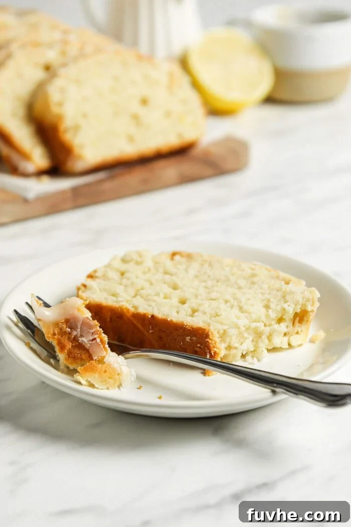 Zesty Vegan Lemon Loaf 8 Slice of lemon drizzle cake with icing on a small plate with a fork.