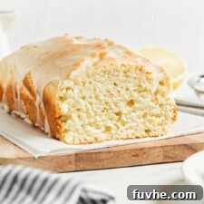 Zesty Vegan Lemon Loaf 9 Sliced lemon pound cake topped with glaze on a cutting board lined with parchment paper.