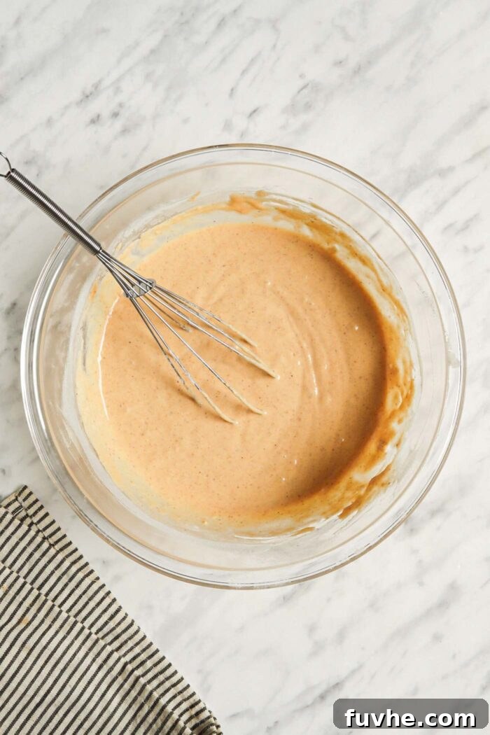 A rich, thick pumpkin pancake batter resting in a mixing bowl, showing its ideal consistency after the dry ingredients have been folded in, with a whisk still in the bowl.