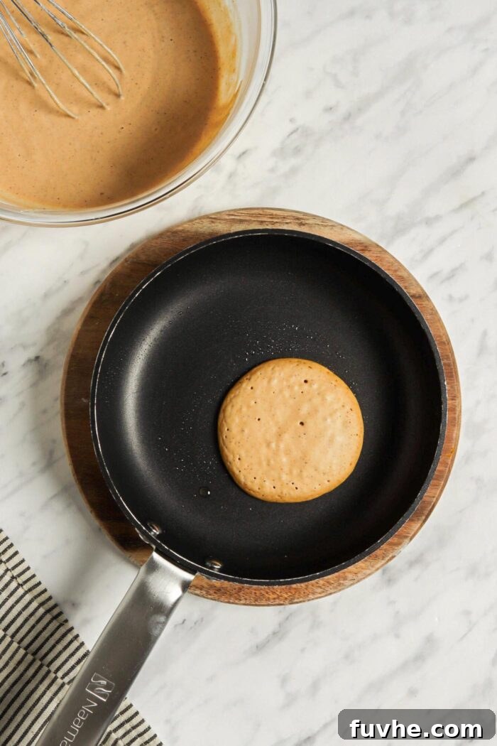 A single perfectly round pumpkin pancake sizzling gently on a hot non-stick skillet, bubbles forming on its surface, indicating it's nearly ready to be flipped.