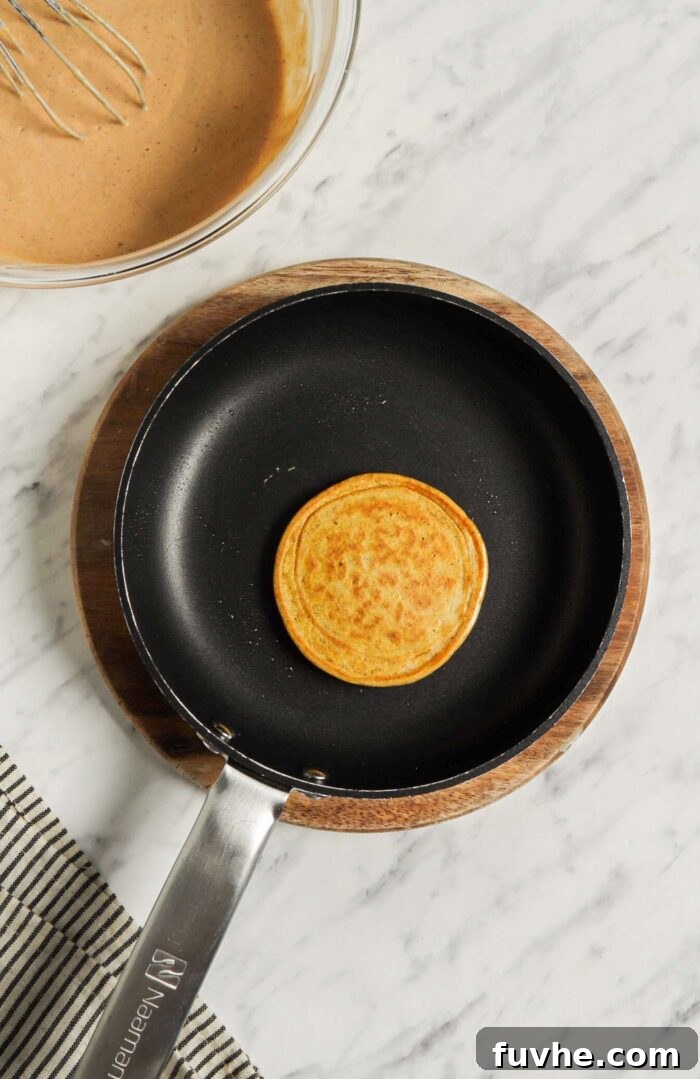 Another view of a single pumpkin pancake expertly cooking on a non-stick skillet, showcasing its golden-brown underside after being flipped.