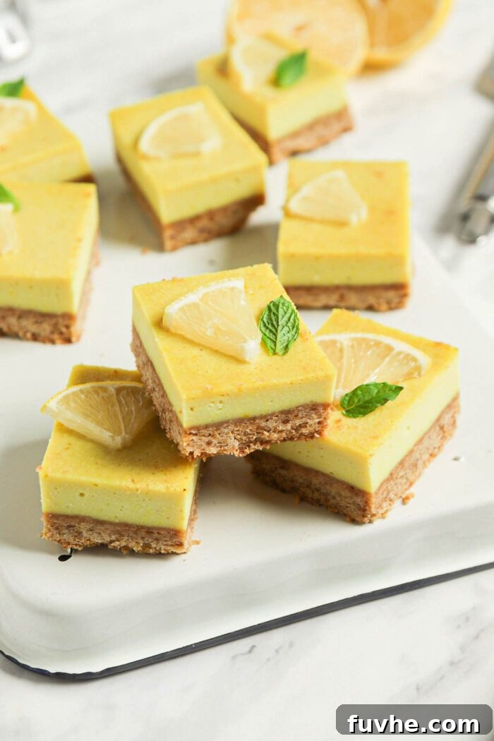 Three perfectly cut vegan lemon squares stacked on an upside down baking tray, with more lemon bars visible in the blurred background on a marble surface.