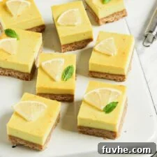 Numerous vegan lemon squares on an upside down baking tray on a marble surface, with a slice of lemon and a lemon zester in the background, beautifully arranged.