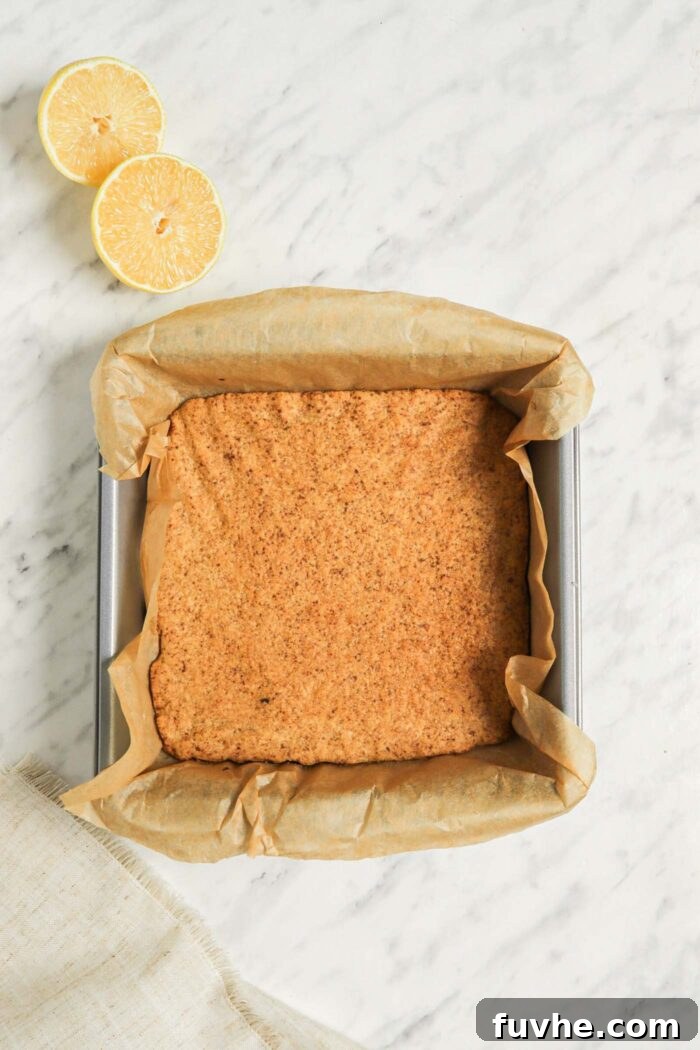 A golden brown, perfectly baked shortbread crust sitting in a square baking dish lined with parchment paper, cooling down on a wire rack.