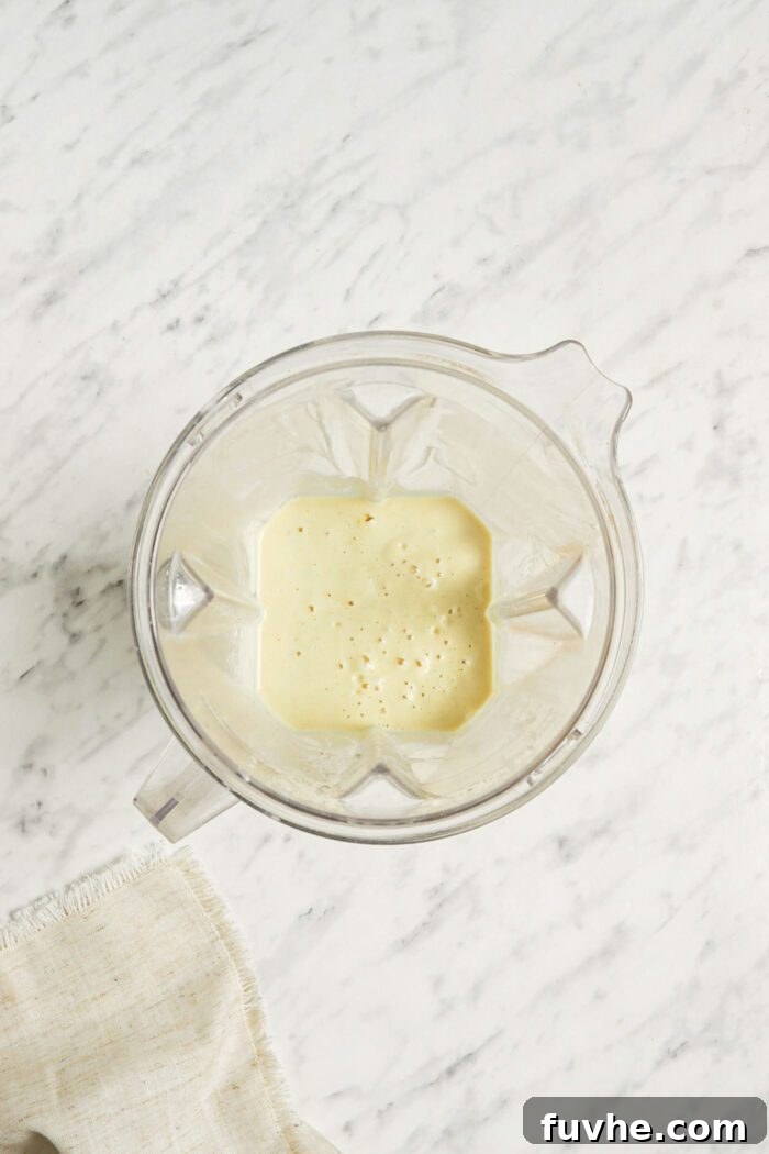 A rich, creamy lemon bar filling mixture swirling smoothly in a blender container, ready to be poured over the cooled crust.