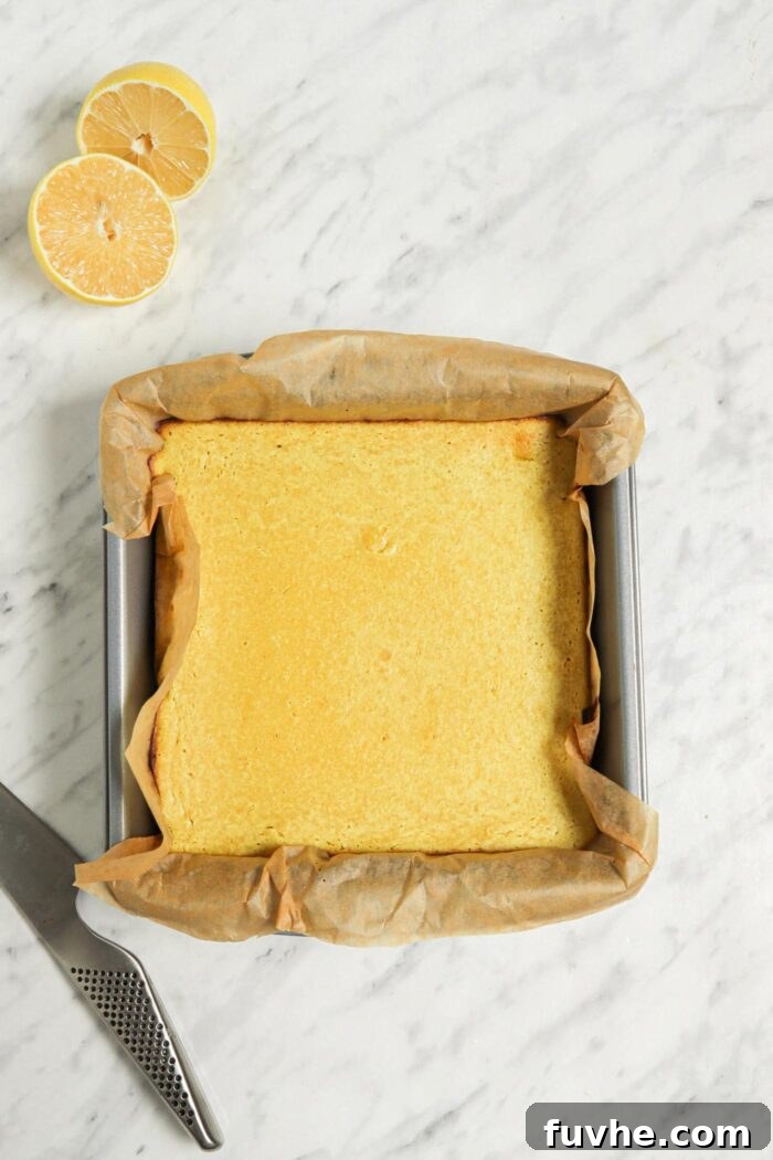 Freshly baked vegan lemon bars in a square metal baking pan lined with parchment paper, glistening and perfectly set, with a slight golden hue.