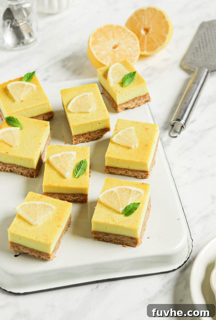 Numerous perfectly cut vegan lemon squares arranged on an upside down baking tray on a marble surface, with a slice of lemon and a lemon zester in the background, showcasing their vibrant color.