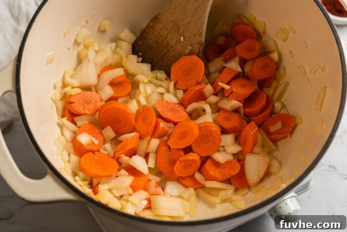 Zesty Lemon Lentil Comfort 4 Chopped onion, garlic, and carrots are gently cooking in a large soup pot, being stirred with a wooden spoon.