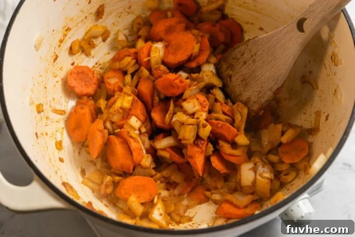Zesty Lemon Lentil Comfort 5 A mix of onions, garlic, carrots, and spices with tomato paste are being stirred in a large soup pot, creating a fragrant base.