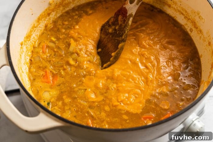 Zesty Lemon Lentil Comfort 7 Half of the red lentil lemon soup has been blended to a creamy consistency, now resting in the soup pot with a wooden spoon.