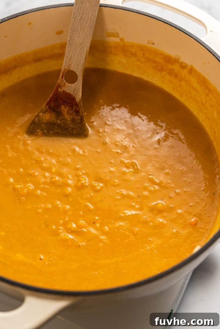 Zesty Lemon Lentil Comfort 8 Rich lemon red lentil soup with turmeric awaits, ready to be served from a large soup pot with a wooden spoon resting inside.
