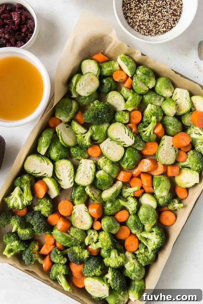Freshly chopped carrots, Brussels sprouts, and broccoli florets, seasoned and spread evenly on a parchment paper-lined baking pan, ready for roasting.