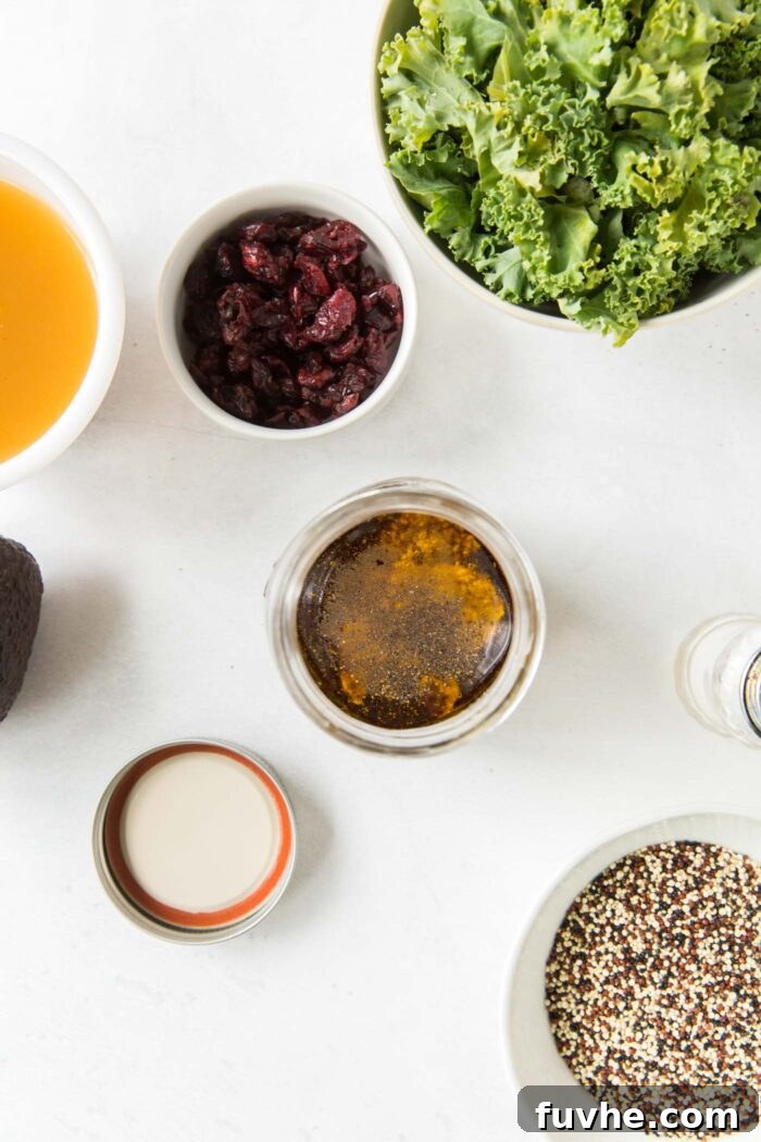 An overhead shot showcasing a small jar filled with freshly made maple balsamic dressing, alongside a bowl of vibrant chopped kale and a separate bowl of perfectly cooked quinoa.