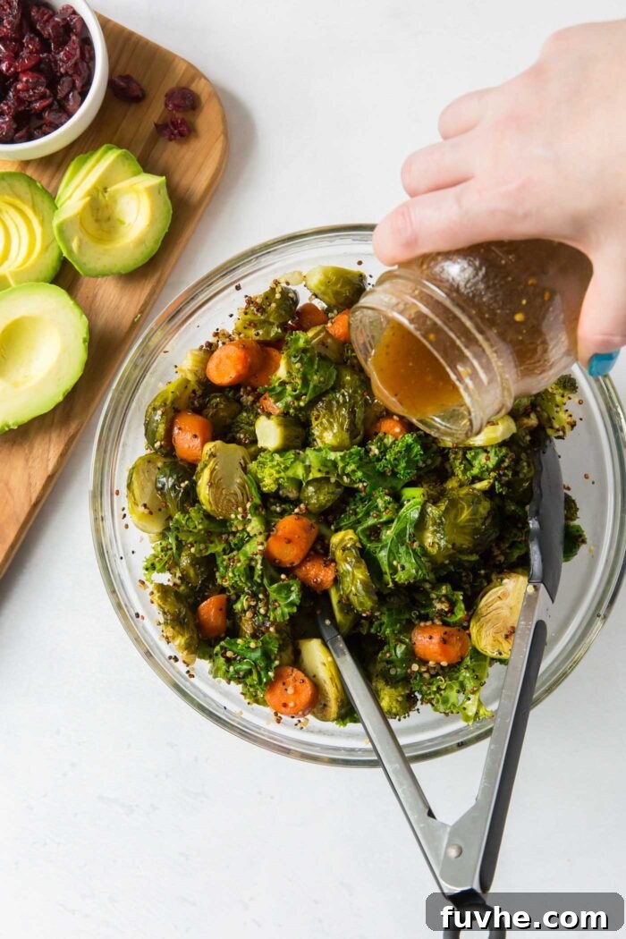A hand gently pouring a rich balsamic dressing over a colorful mix of kale, roasted carrots, and Brussels sprouts, ready to be tossed into a satisfying quinoa salad.