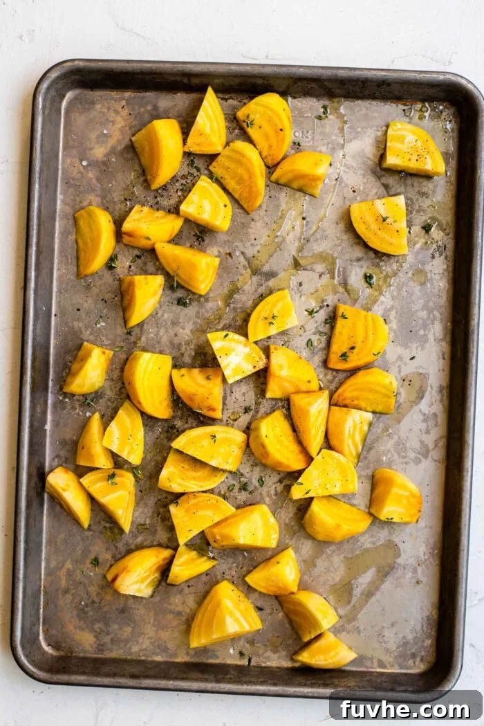 Chopped and peeled golden beets on a baking pan, drizzled with olive oil and herbs, spread in a single layer.