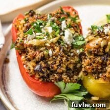 Two Mediterranean quinoa stuffed bell peppers topped with feta and parsley on a plate.