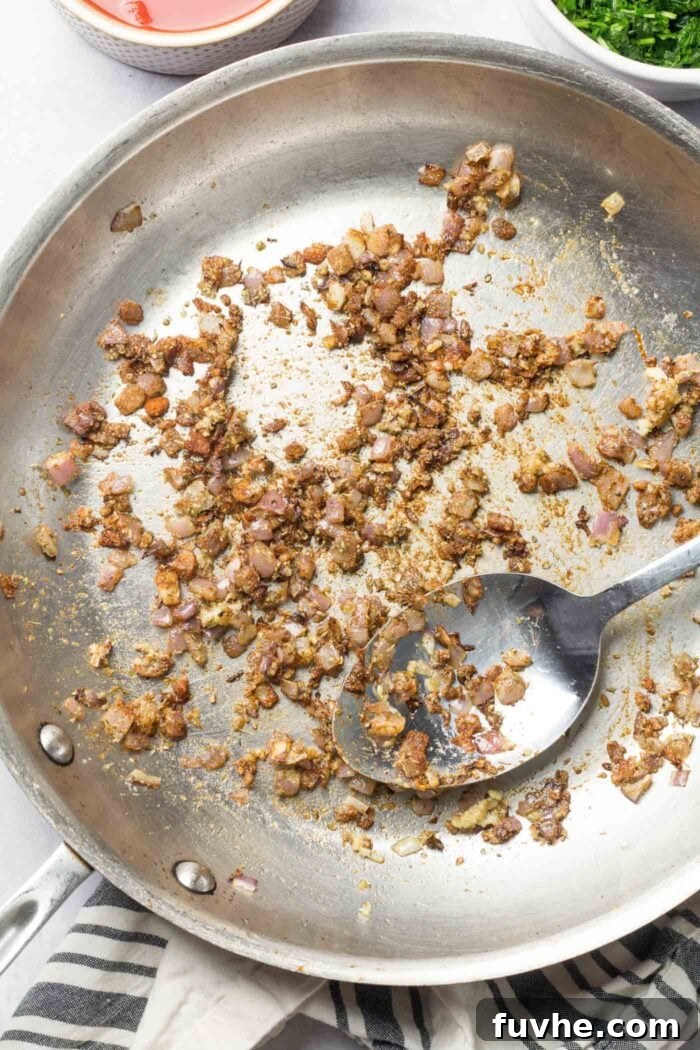 Minced garlic and diced red onion gently cooking in a hot skillet with a metal spoon, releasing their aromatic flavors.