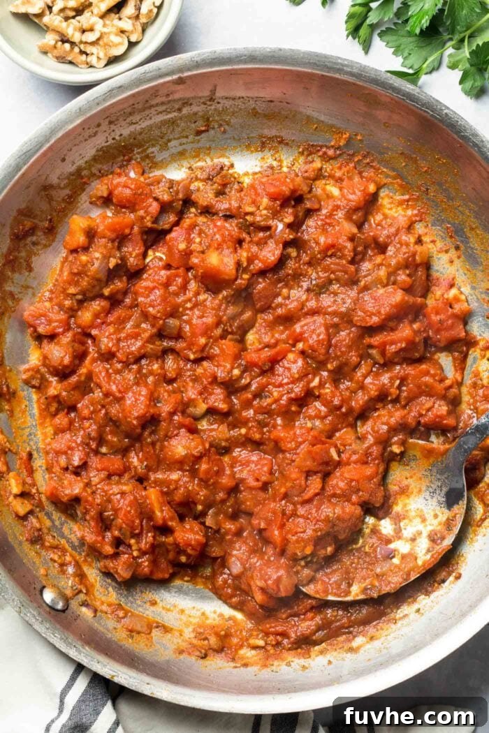 Tomato paste, diced tomatoes, onion, and garlic simmering together in a hot skillet, creating a rich and flavorful sauce base.