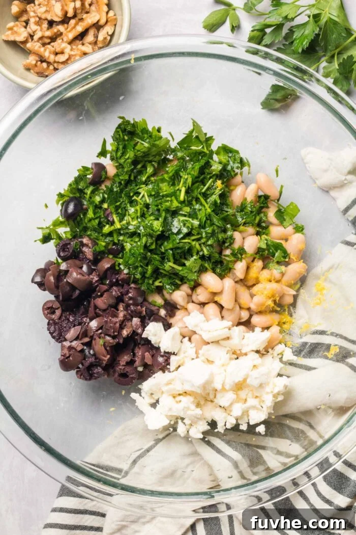 A large mixing bowl filled with vegan feta, fresh parsley, white beans, lemon zest, lemon juice, and Kalamata olives, ready to be combined.