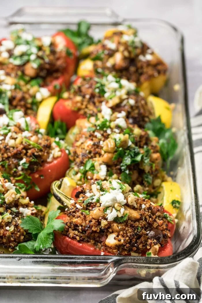 A casserole dish showcasing beautifully baked, halved stuffed bell peppers, generously filled with a quinoa and bean mixture and topped with crumbled vegan feta.