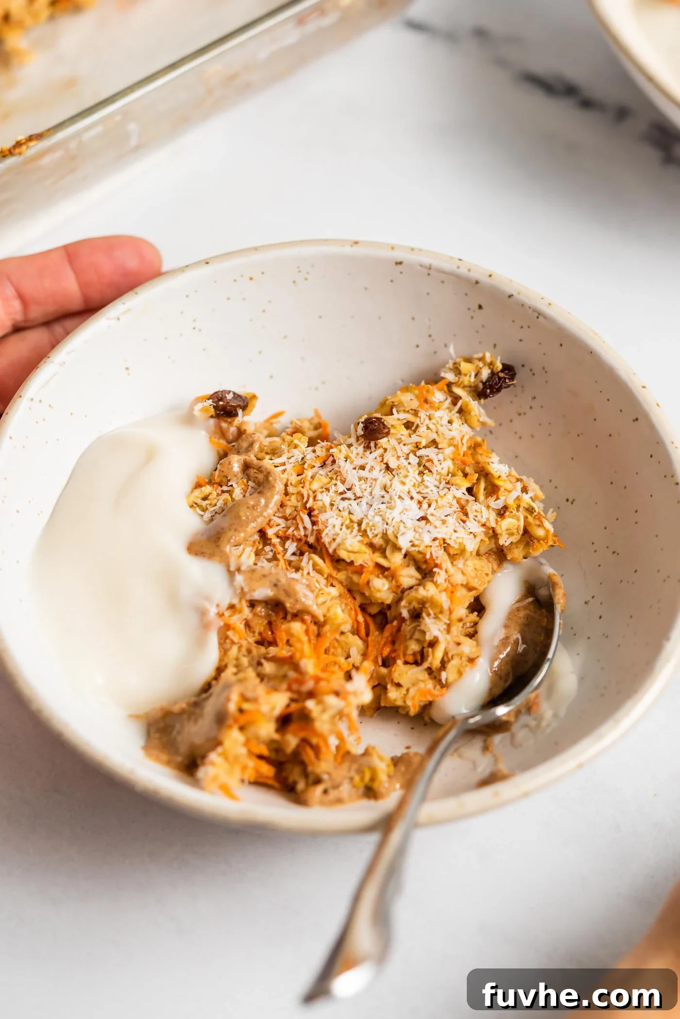 A beautifully presented bowl of carrot cake baked oatmeal, garnished with creamy yogurt and a swirl of rich almond butter, ready for a delicious start to the day.