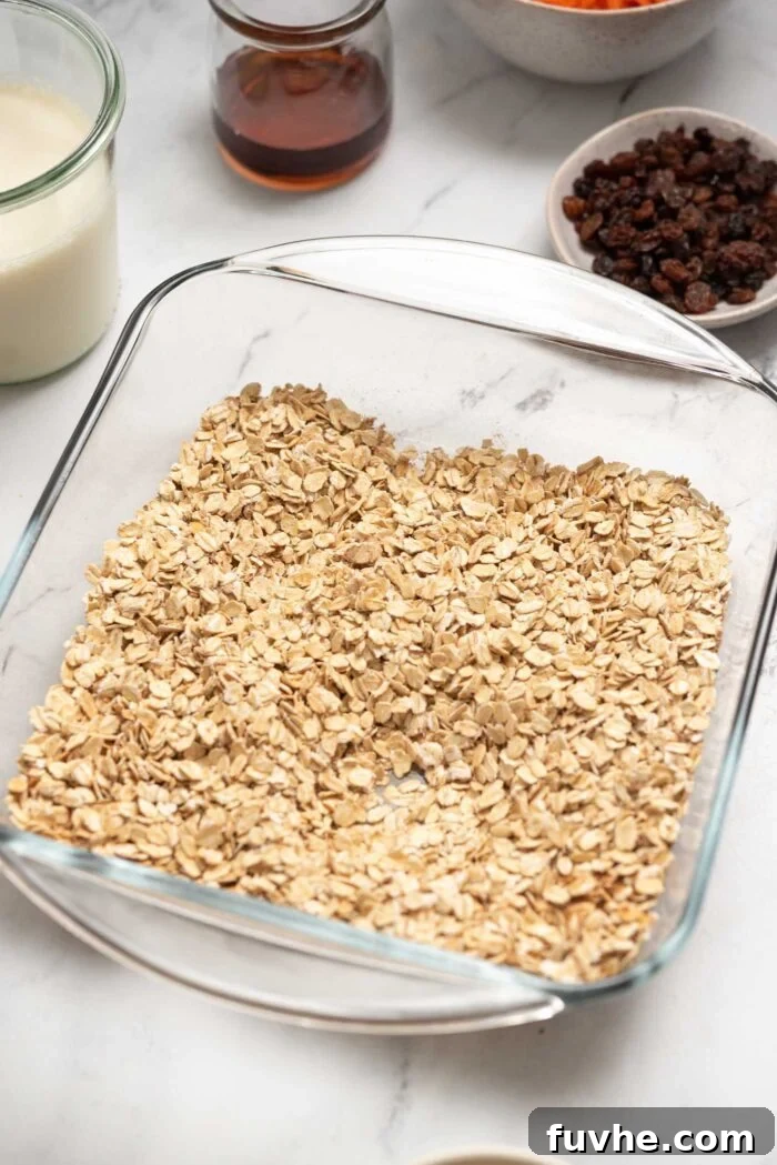 A close-up of rolled oats evenly spread in a square glass baking dish, forming the base for the baked oatmeal.