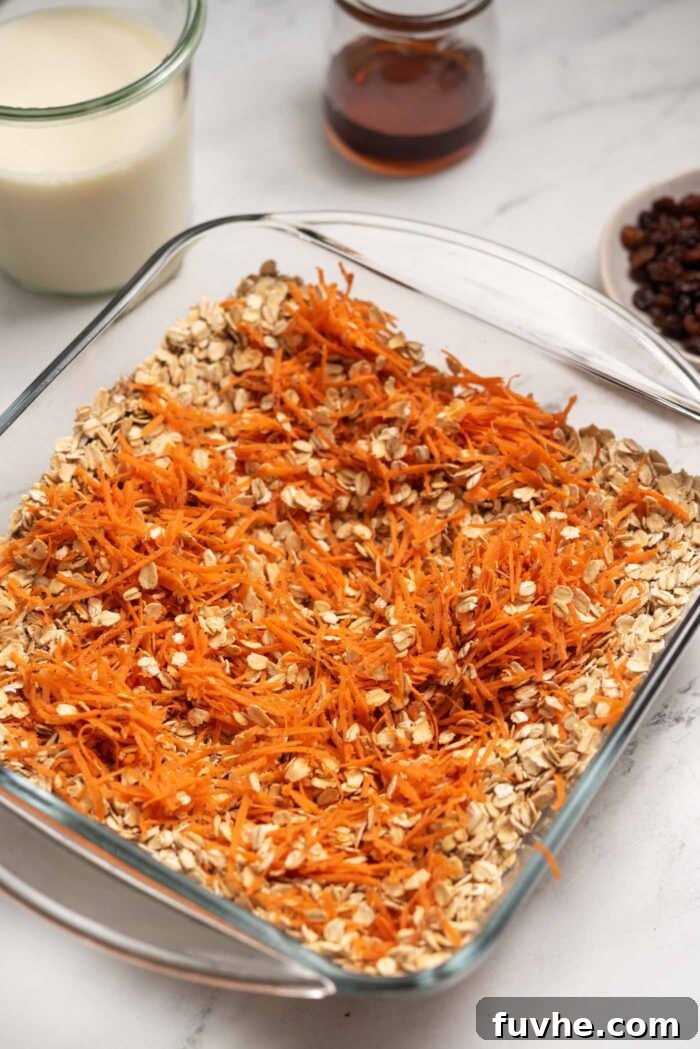 Finely grated carrots mixed thoroughly with rolled oats in a square glass baking dish, showcasing the vibrant color and even distribution.