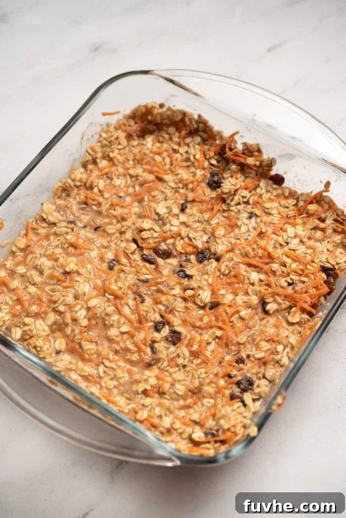 The fully mixed carrot cake baked oatmeal batter, studded with walnuts, raisins, and grated carrot, ready for baking in a square dish.