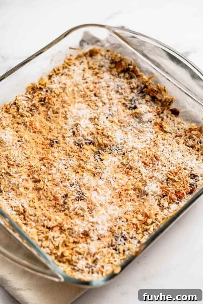 A baked dish of carrot cake oatmeal, golden-brown and topped with toasted coconut, glistening and ready to be served.
