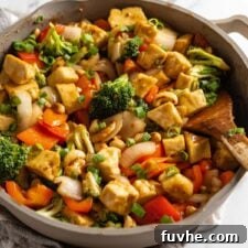 A cashew tofu vegetable stir fry in a large skillet on a marble surface.