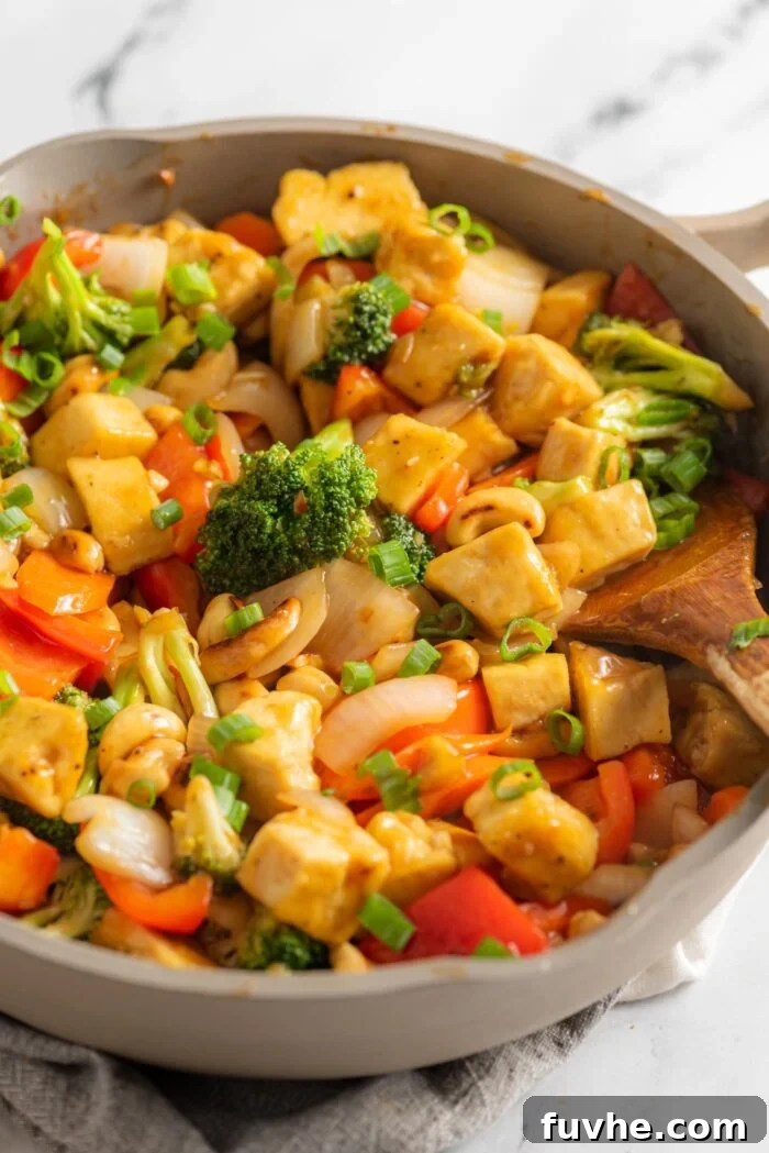 A cashew tofu broccoli stir fry in a large skillet on a marble surface.