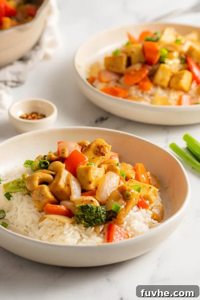 Cashew tofu stir fry with broccoli and peppers served over rice on a plate. Another plate of stir fry is in the background.