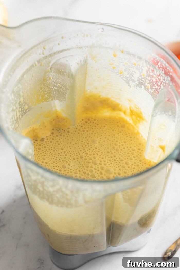 A vibrant yellow vegan egg batter, artfully crafted from a blend of tofu and chickpea flour, swirling smoothly within a blender container, ready for the next step of the recipe.