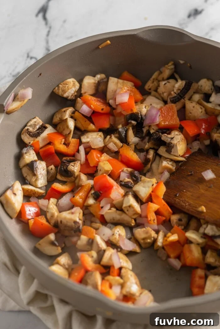 A colorful mixture of mushrooms, red onion, and red bell pepper gently cooking in a non-stick skillet, stirred occasionally with a wooden spoon until perfectly softened and aromatic.