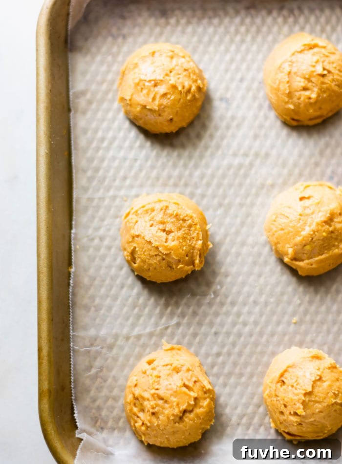 No-Bake Vegan Peanut Butter Chocolate Truffles 6 Small, uniformly rolled balls of peanut butter dough cooling on a baking tray lined with parchment paper, prepped for dipping.