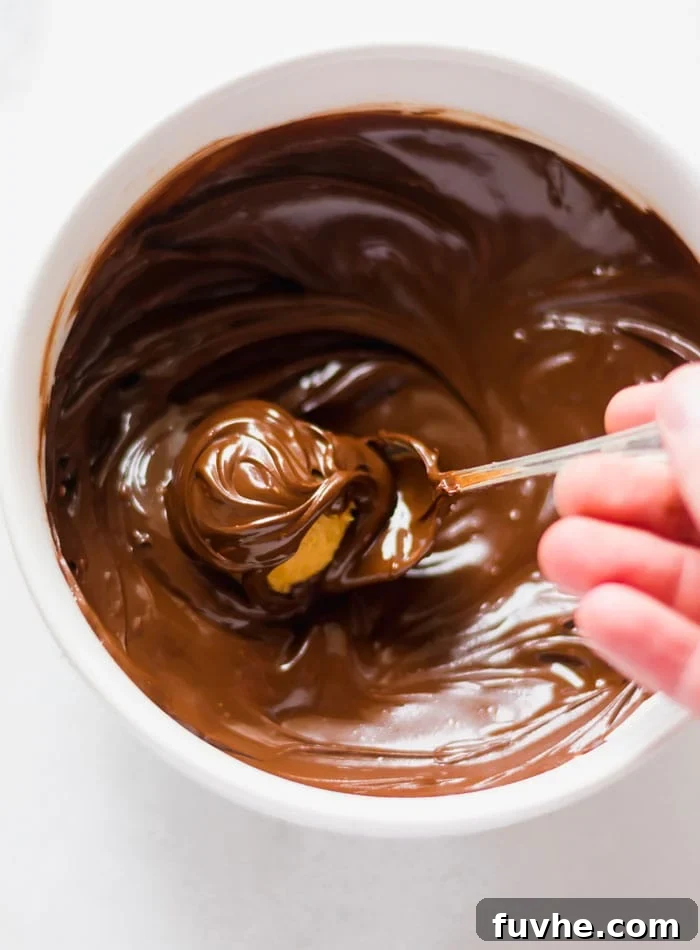 No-Bake Vegan Peanut Butter Chocolate Truffles 8 A peanut butter ball being carefully lowered into a bowl of perfectly melted chocolate, showcasing the dipping process.