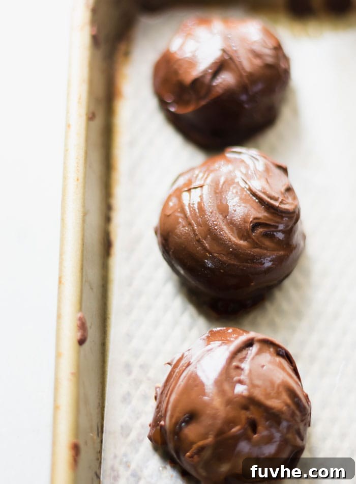 No-Bake Vegan Peanut Butter Chocolate Truffles 9 Three freshly chocolate-covered peanut butter balls, still wet from dipping, arranged on a baking tray lined with parchment paper.