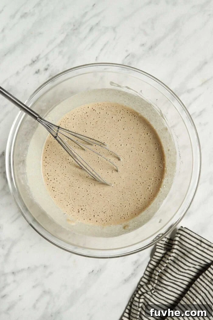 A bowl filled with smooth, pale buckwheat crepe batter, with a whisk resting inside. The batter appears perfectly mixed and ready for cooking.