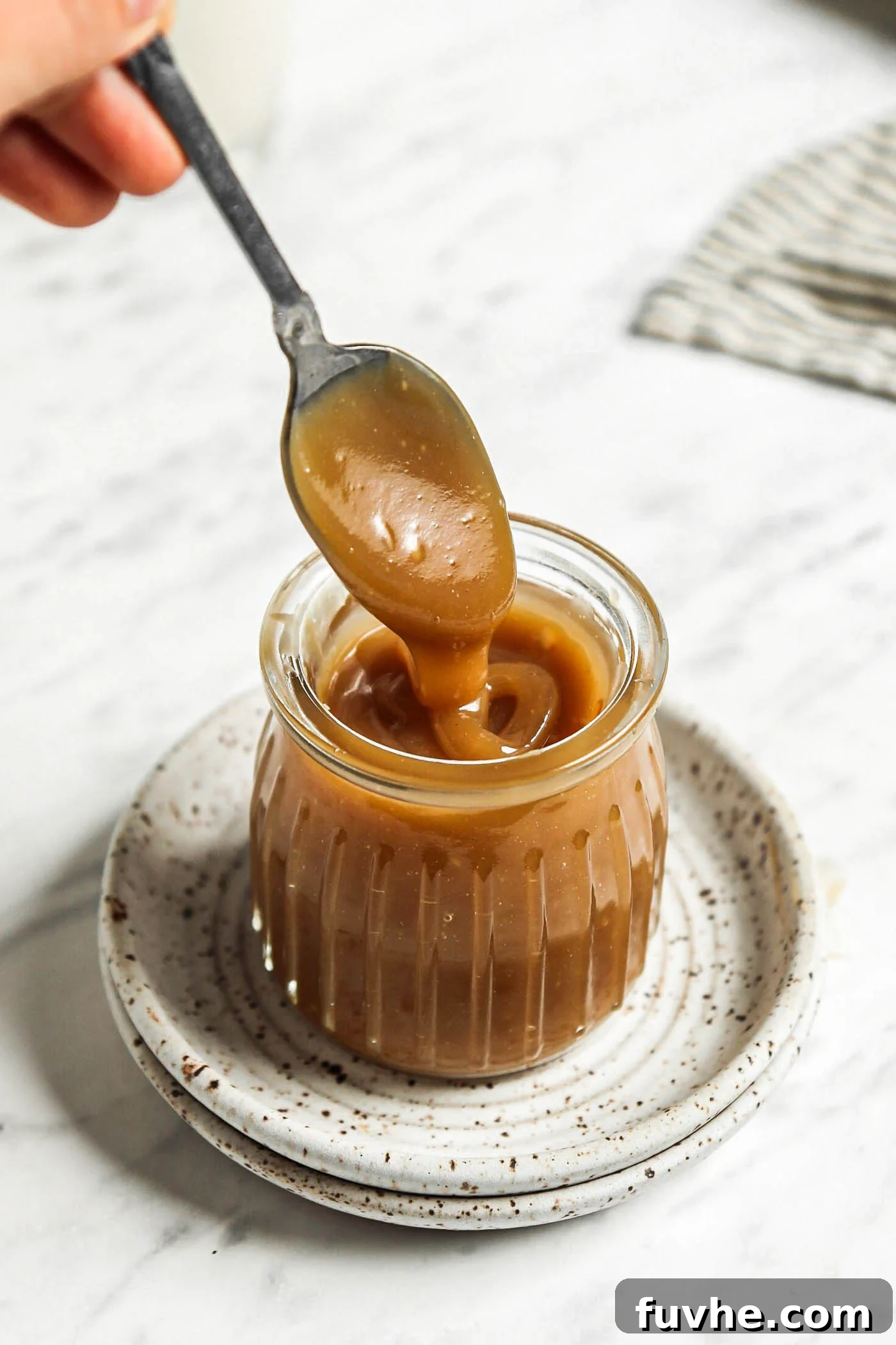 Spoon dipping into a small jar of homemade vegan caramel sauce, highlighting its thick and creamy texture.