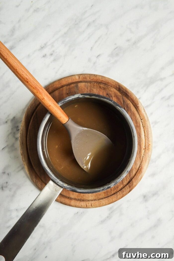 Thick, dark caramel in a medium saucepan with a wooden spoon, indicating it's nearly ready.