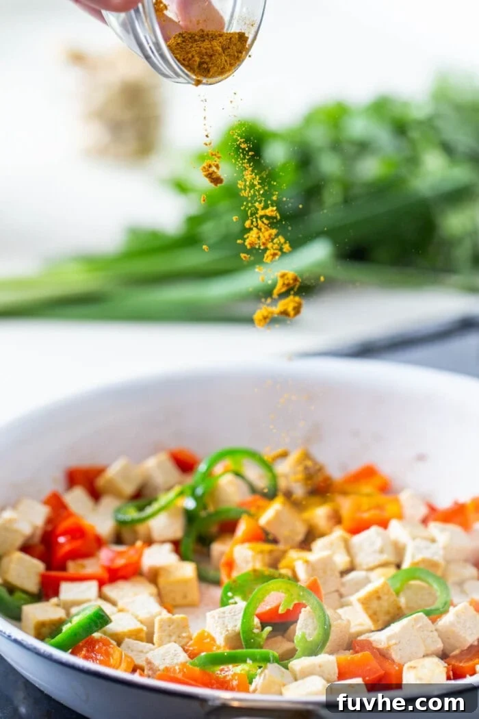 Curry powder being sprinkled into a skillet of tofu and veggies.