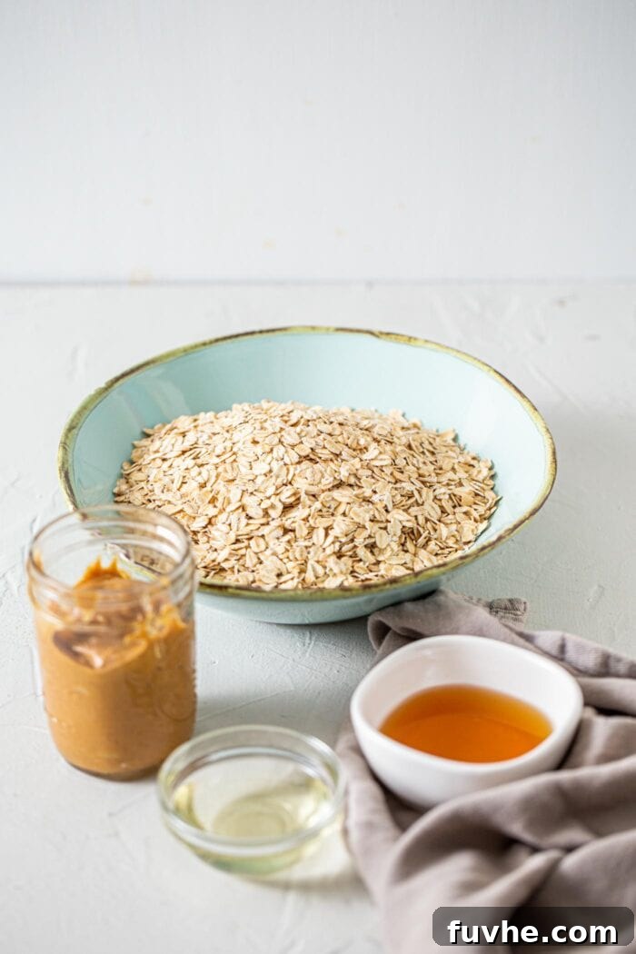 Oats, maple syrup, coconut oil and peanut butter in containers on a countertop.